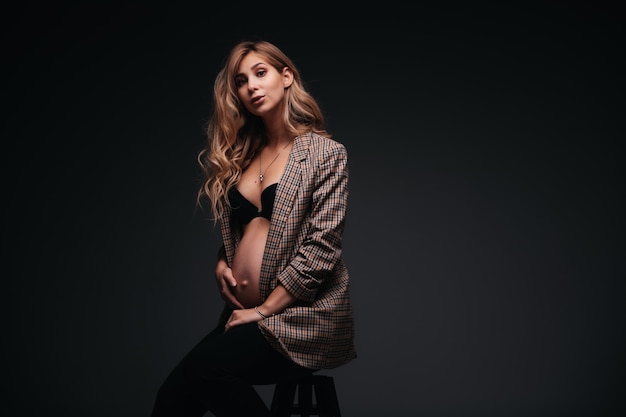 Young beautiful pregnant woman in jacket on black wall