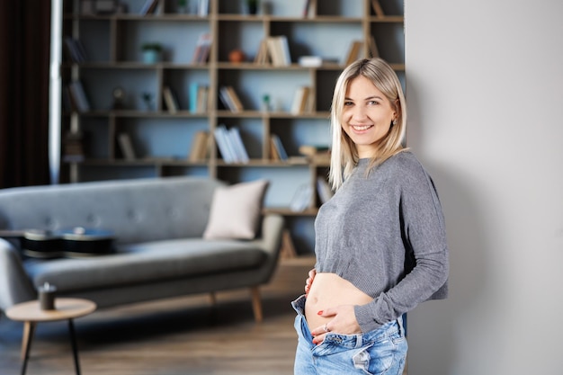 Young beautiful pregnant woman standing near the wall at home