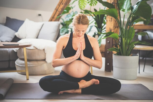 Young beautiful pregnant woman training yoga at home in her living room motherhood pregnancy