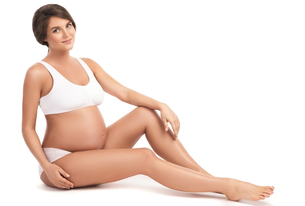 Young and beautiful pregnant woman on white wall