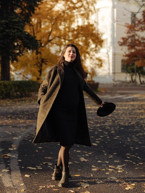 Young beautiful pregnant woman with dark hair in a black tight dress and coat posing