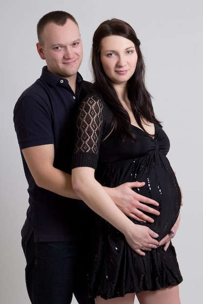 Young beautiful pregnant woman with husband over grey background