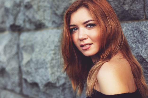 Young beautiful red-haired girl looks around. gray wall background.