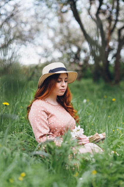 Young beautiful red-haired girl walks in a spring blooming apple orchard