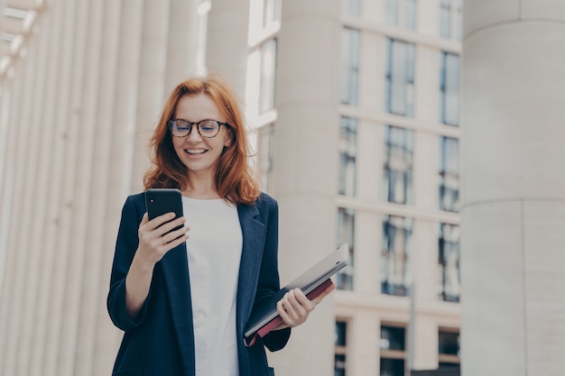 興奮した表情でスマートフォンを見ている若い美しい赤毛の女性最高経営責任者