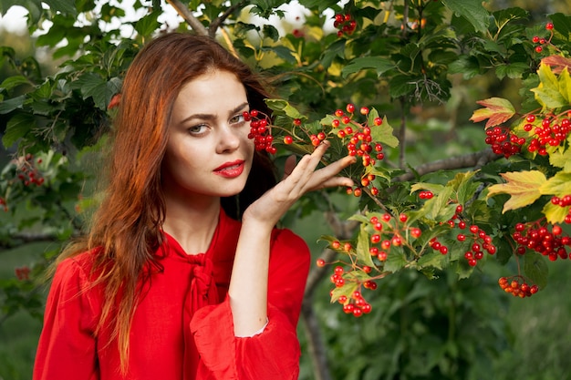 自然の中で緑の茂みの植物を背景にポーズをとって若い美しい赤毛の女性