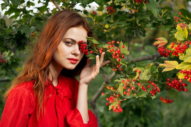 Молодая красивая рыжая женщина позирует на фоне зеленых кустовых растений в природе
