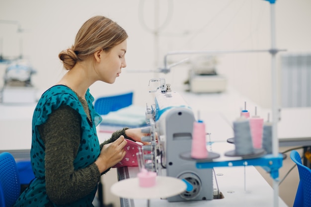 Young beautiful seamstress sews on sewing machine in factory