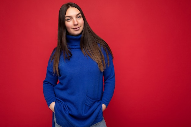 Young beautiful self-confident brunette woman with sincere emotions isolated on background wall with copy space wearing casual trendy blue sweater. Positive concept