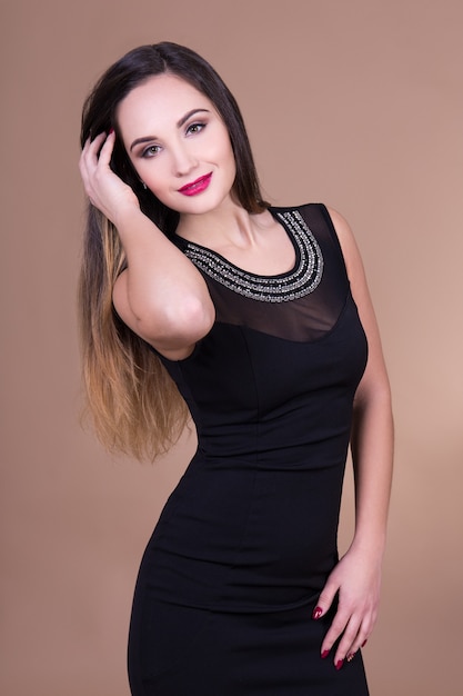 Young beautiful sexy woman in black dress posing over beige background
