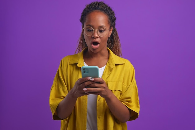 Young beautiful shocked african american woman with phone in hands opens mouth