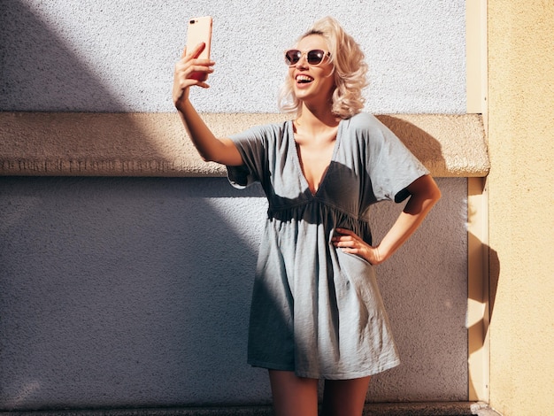 young beautiful smiling blond woman in trendy summer dress clothes model in the street takes selfie