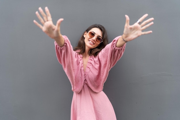 Young beautiful smiling cute romantic woman in trendy summer dress Carefree woman posing in the street near grey wall Positive model outdoors in sunglasses Cheerful and happyxA