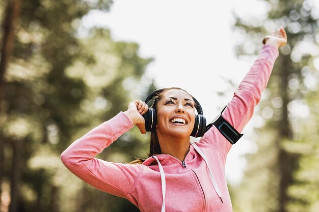 Young beautiful smiling female runner listening to music and preparing to jogging outdoor.