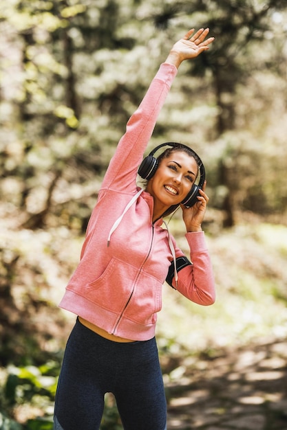 Photo young beautiful smiling female runner listening to music while stretching after jogging in nature.