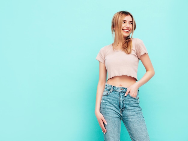 Young beautiful smiling female in trendy summer clothes carefree woman posing near blue wall in studio Positive brunette model having fun Cheerful and happy