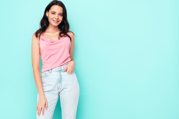 Young beautiful smiling female in trendy summer clothes Sexy carefree woman posing near blue wall in studio Positive brunette model having fun and going crazy Cheerful and happy