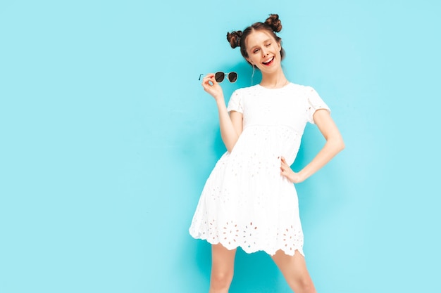 Young beautiful smiling female in trendy summer dress Sexy carefree woman with two horns hairstyle posing near blue wall in studio Positive model having fun