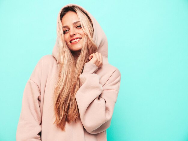 Young beautiful smiling female in trendy summer hoodie Sexy carefree woman posing near blue wall in studio Positive blond model having fun and going crazy Cheerful and happy