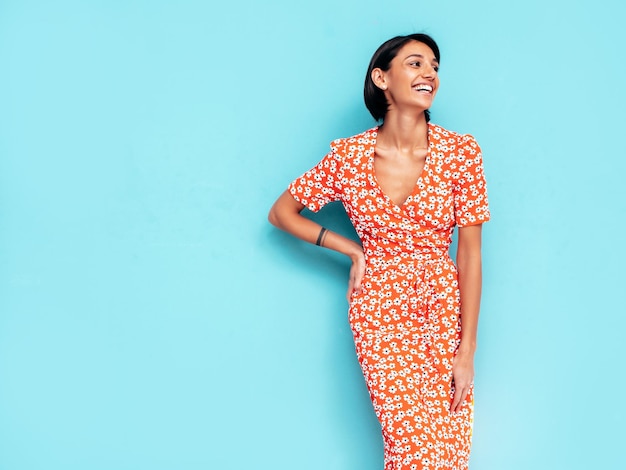 Young beautiful smiling female in trendy summer red dress Sexy carefree woman posing near blue wall in studio Positive model having fun Cheerful and happy Isolated