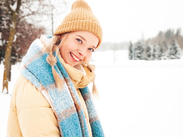 Young beautiful smiling hipster female in trendy warm clothes and scarf.Carefree woman posing in the street in park. Positive pure model having fun in snow. Enjoying winter moments