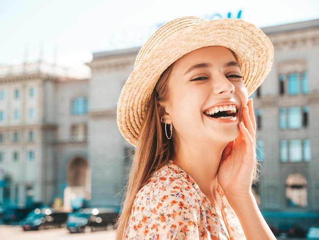 Young beautiful smiling hipster woman in trendy summer dress Sexy carefree woman posing on the street background in hat at sunset Positive model laughing outdoors Cheerful and happy