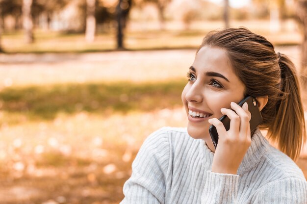 公園で携帯電話で話している若い美しい笑顔の女性。