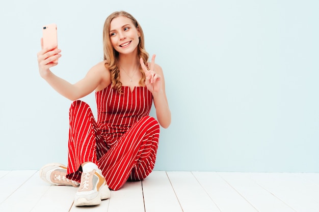 Young beautiful smiling woman in trendy summer clothes. Sexy carefree woman posing near light blue wall in studio