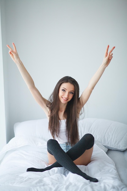 Giovane bella donna sorridente che si sveglia in camera da letto bianca