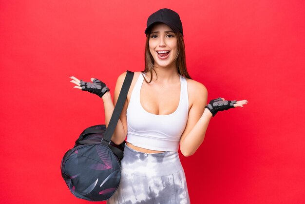 Young beautiful sport woman with sport bag isolated on red background with shocked facial expression