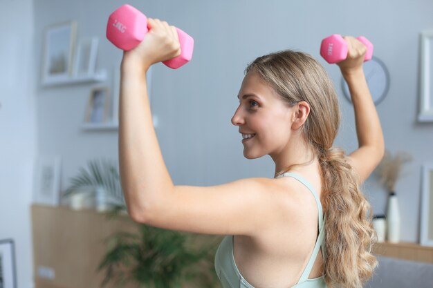 Young beautiful sports girl in leggings and a top does exercises with dumbbells. Healthy lifestyle. A woman goes in for sports at home.