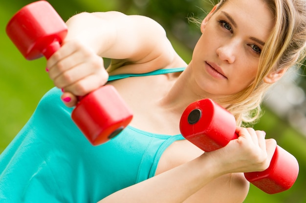 Young beautiful sports girl with dumbbells in the park on a background of green grass