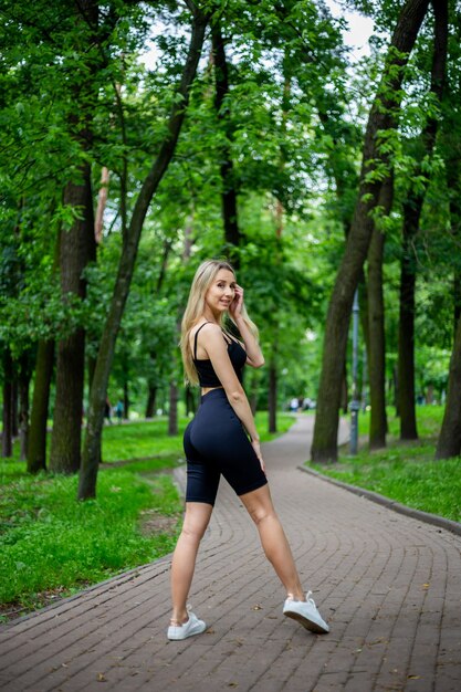молодая красивая спортивная блондинка в хорошей форме позирует перед зелеными деревьями на природе