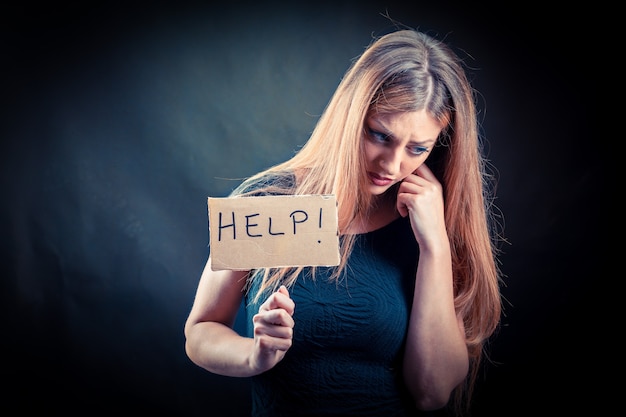 Young beautiful and stressed blonde woman holding help sign isolated on dark background