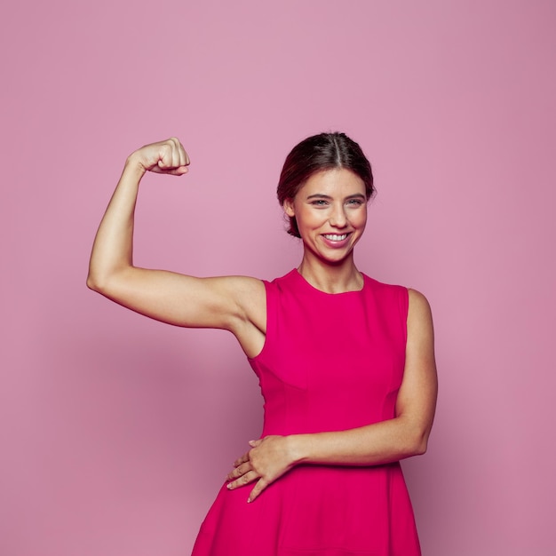 Young beautiful strong woman standing over pink background and showing arm muscle Women power concept