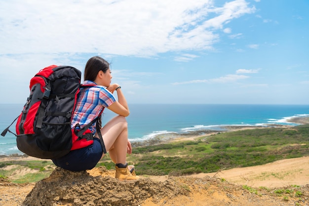 Young beautiful student going to sea island country travel and
climbing mountain sitting on hill top enjoy sea scenery day
dreaming about future with sky.