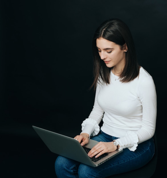 Young beautiful student woman working on laptop over dark background