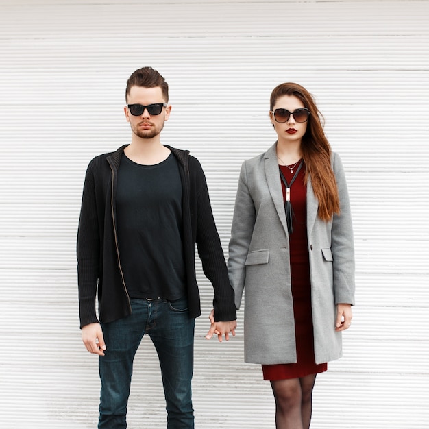 Photo young beautiful stylish couple in fashionable clothes stand near white wooden wall