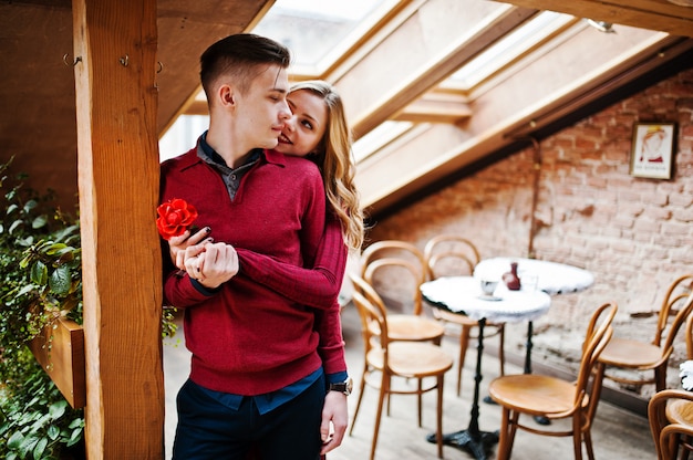 屋根の大きな窓とビンテージカフェで愛の物語の赤いドレスを着た若い美しいスタイリッシュなカップル