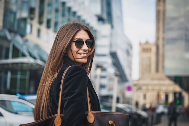 Young beautiful stylish girl in Sunglasses walking on street. Close up portrait of woman is turn around at camera and smiles.