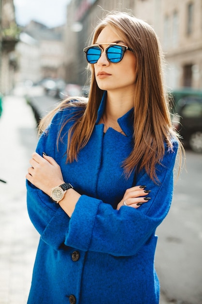 青いコートの秋のファッショントレンドで通りを歩く若い美しいスタイリッシュな女性