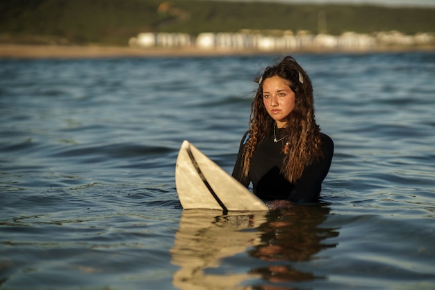 Young beautiful surfer female on the beach at sunset