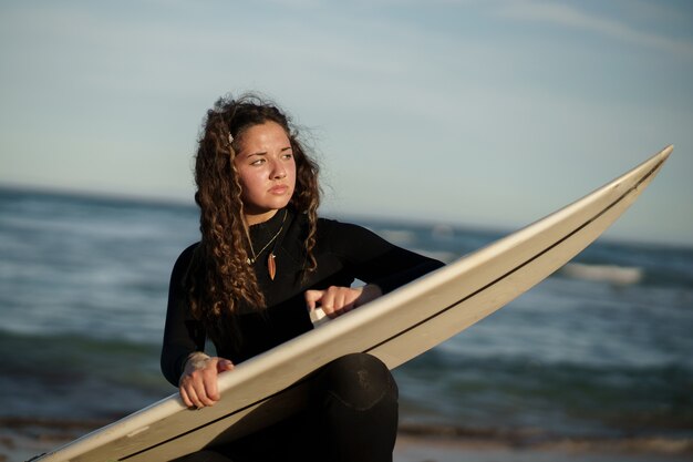 Young beautiful surfer female on the beach at sunset