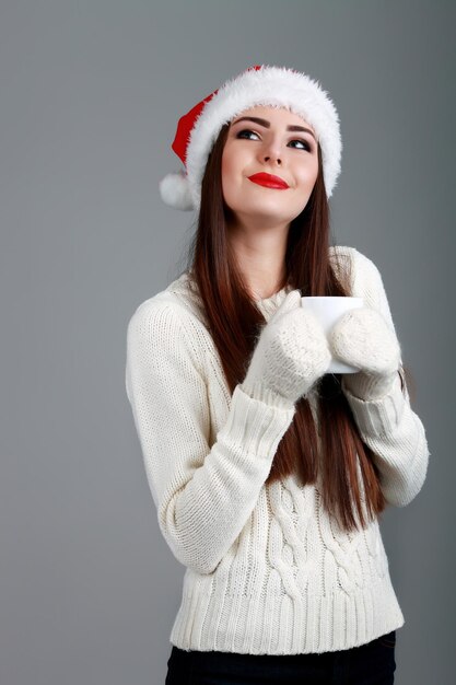 Giovane e bella adolescente in cappello da babbo natale con una tazza di caffè calda