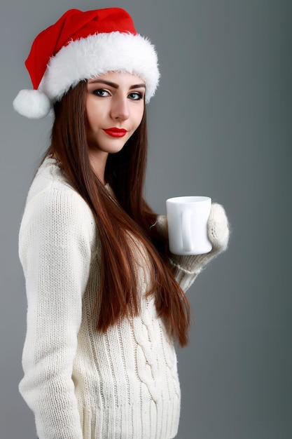 Giovane e bella adolescente in cappello da babbo natale con una tazza di caffè calda