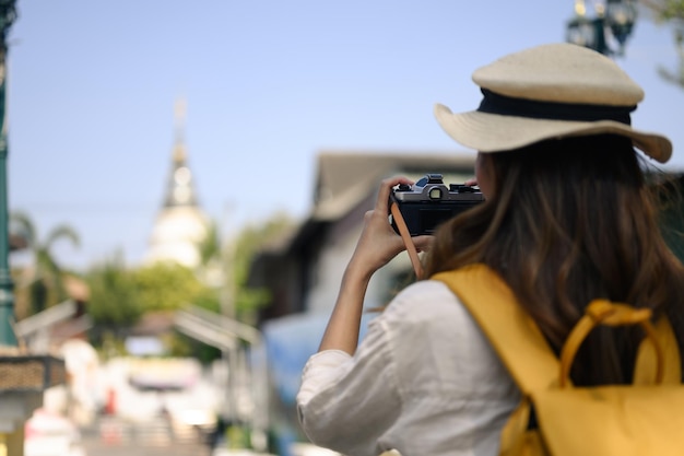 背包を背負った美しい若い観光客がタイのチアンマイの地元の街をカメラで写真を撮っている