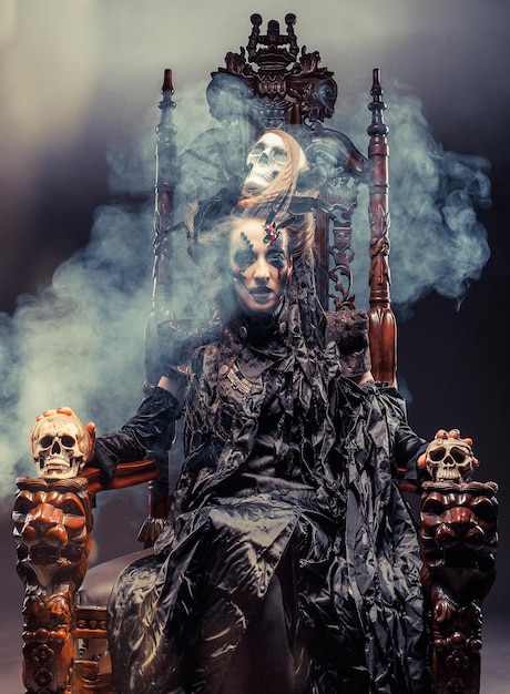 Young beautiful witch sits on a chair Bright make up skull smoke halloween theme