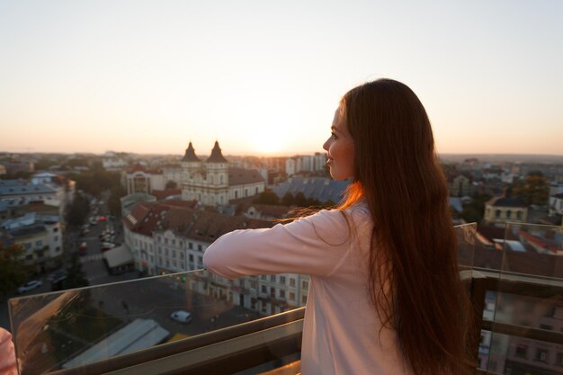 Young beautiful woman admiring panoramic view of european street architecture high from the balcony