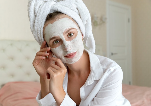 Young beautiful woman apply face mask in bedroom