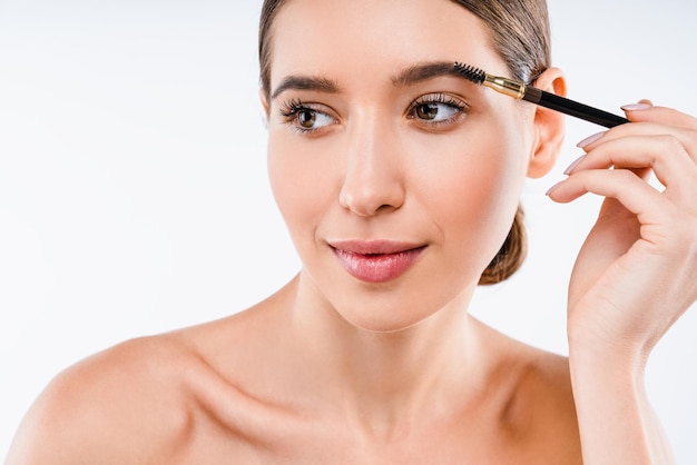 Young beautiful woman applying cosmetic brush on eyebrow natural makeup on white background